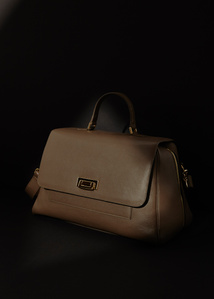 Tan brown leather gold plated buckle and gold zipper designer handbag by ectu placed in the shadows with dark background with a small portion of the bag partially lit.
