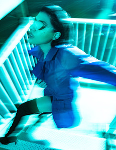 moody colorful portrait brunette female model standing on white stair well wearing blue coat and sunglasses black boots with blurry motion movement