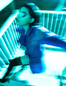 brunette female model standing on white stair well wearing blue coat and sunglasses black boots with blurry motion 