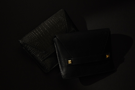 Black leather clutch designer ectu purses sitting on top of each other on  a black surface with a dark background basking in soft low light