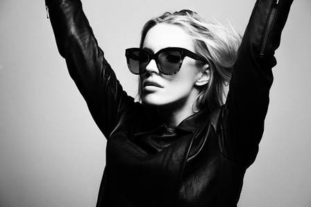 Chloe Holmes woman model arms raised over head blonde hair blowing fair skin wearing black sunglasses black leather jacket in front of white grey background photographed by william gormley