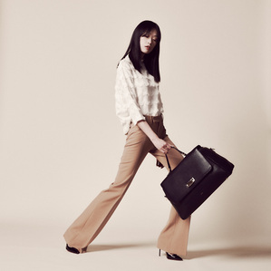 asian woman model dark brown hair wearing white top brown bell bottom pants swinging black leather hand travel bag standing in front of cream white backdrop photograph by william gormley