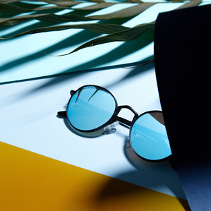 blue mirrored lens sunglasses with black metal frame placed by palm leaf and gold and blue paper surfaces