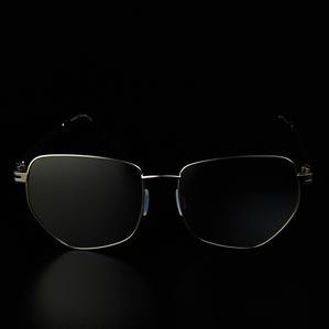 Angular stainless steel rimmed mirrored lens sunglasses sitting on a black surface with a dark background in soft light