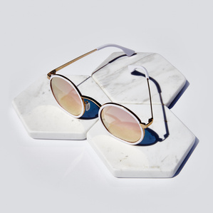 Round gold rimmed mirrored pink multicolor lens sunglasses placed on top of white tiles on white surface in bright light source