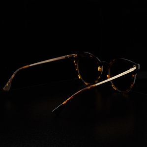 gold metal tortoise rimmed dark lens sunglasses sitting on a black surface with a dark background in soft light