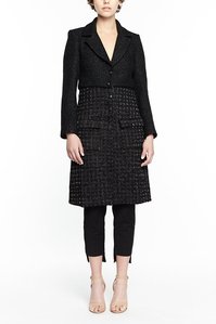 female model with top of face cropped out standing in front a white background wearing an black designer luxury field coat black pants 