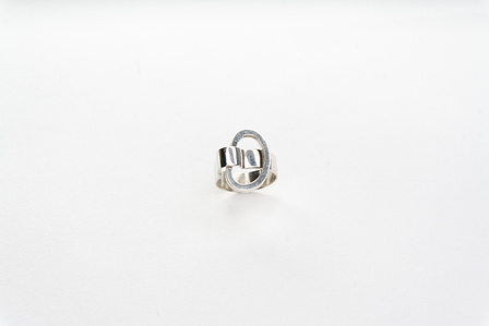 A minimal silver ring is pictured in tilted top view on a neutral white ground. The ring has its own oblong ring shape integrated.