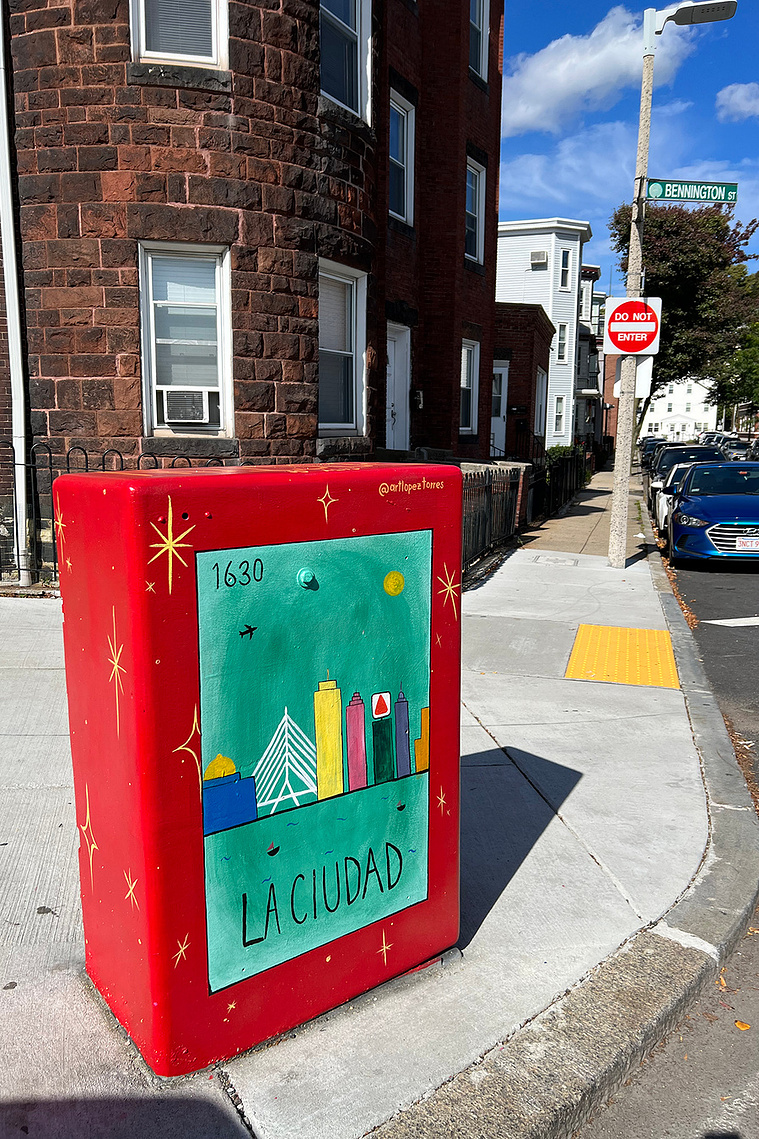 Image of red painted electrical box with green loteria card and graphics of the city of boston that reads 