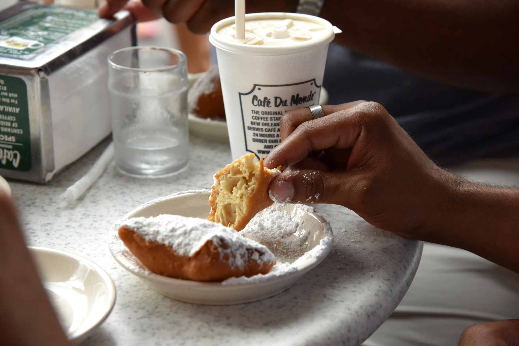 The fingers of Café du Monde first-timer Jordan Costen covered in powdered sugar as he tastes his first beignet. This photo was taken at the Café du Monde location in New Orleans, Louisiana on Tuesday, Aug. 8,2017 (Katherine C. Gilyard/NABJ Monitor)
