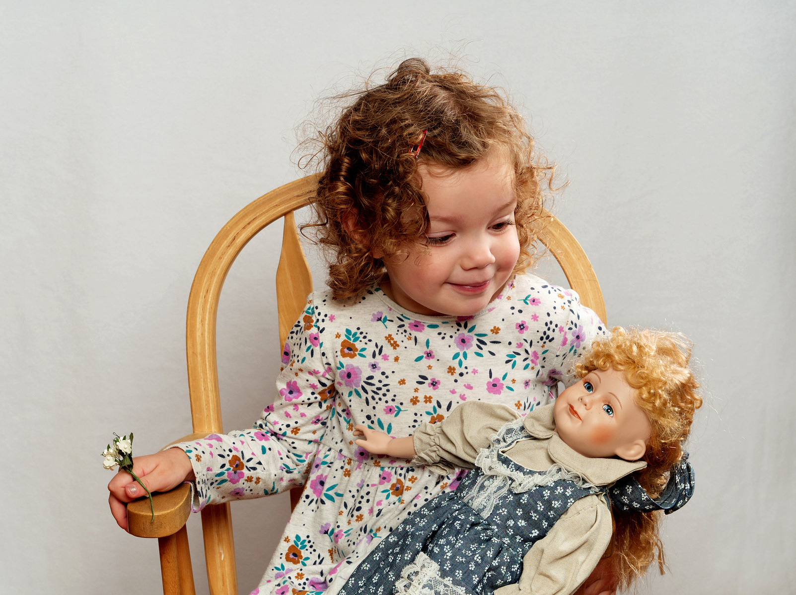 Image Description: "A young toddler posing in a chair with her doll on a white background."