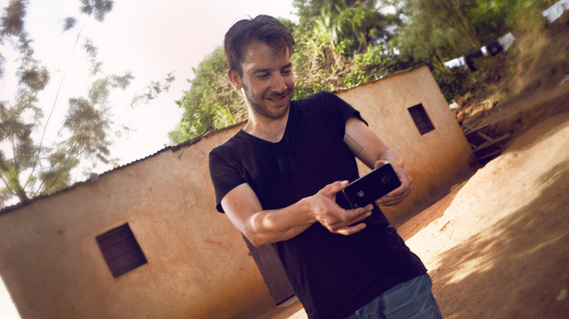 Photographer Gerrit Hahn standing outside in front of a house in Rwanda, taking a picture with his smartphone