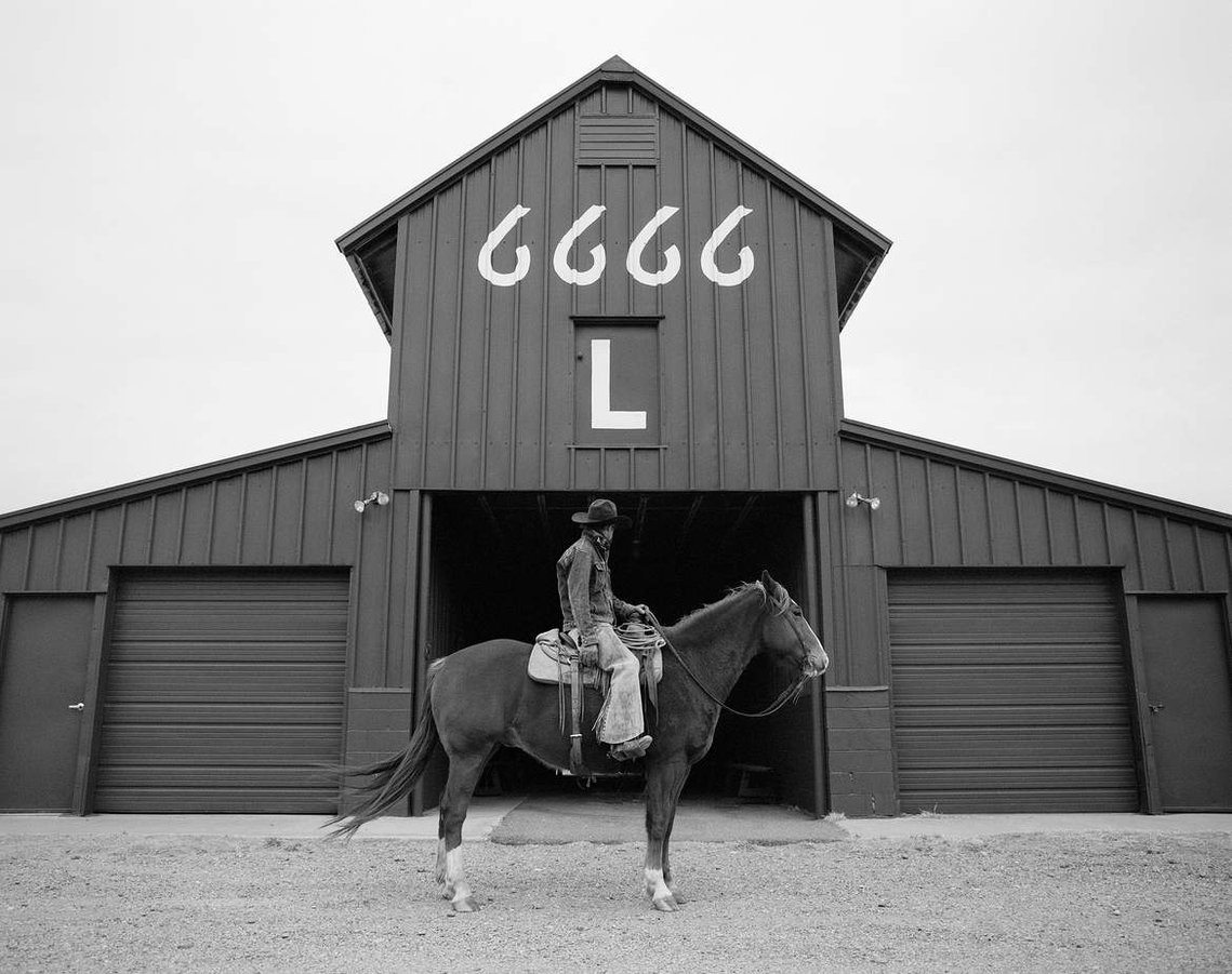 Fine art photograph of the Four Sixes (6666 Ranch) featured in the television show, Yellowstone. Western artwork of cowboy on horseback outside of the Four Sixes barn captured in Texas. The Four Sixes artwork.