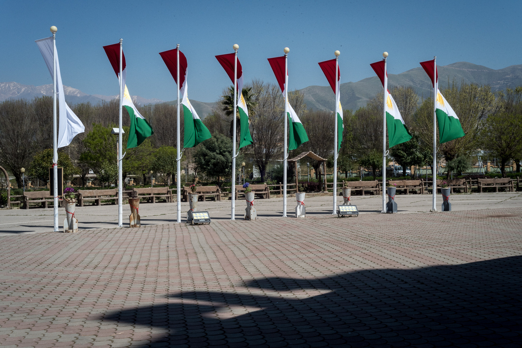 Halabja, KRI. Eight of the sixteen Kurdish flags on display in front of Halabja Monument and Peace Museum are waving in the wind. Below each flag, the original bombs that hit the city, are decorated with flowers as part of an art exhibition to commemorate