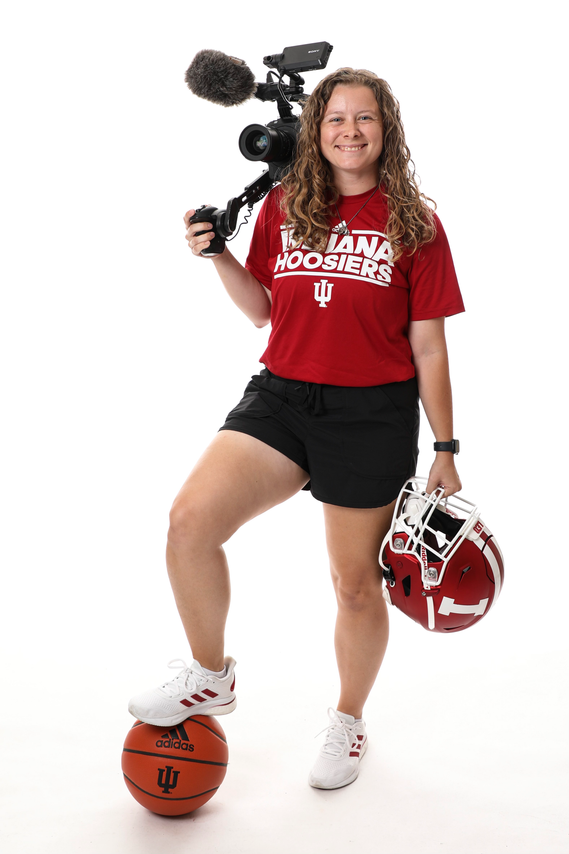 Dani smiles and poses with her right foot on an IU basketball, holding an Indiana football helmet with her left hand, and carrying a video camera on her right shoulder.

Photo by Gracie Farrall/Indiana Athletics