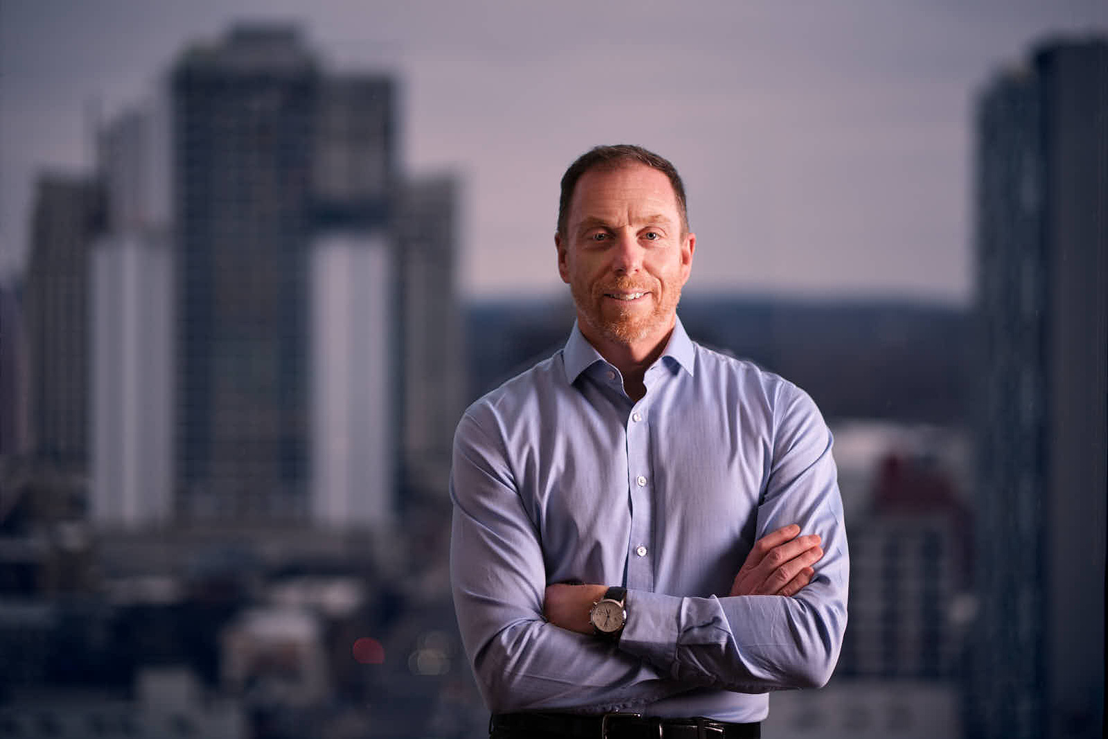 Professional headshot of Trevor Delaire in London, Ontario, an advisor at TD Wealth, wearing a blue shirt, smiling confidently against a blurred indoor background. Photographed by Paul Lambert.
