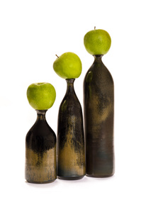 Still life of three brown earthenware vases of different heights, each topped with a green apple.