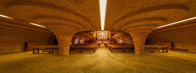 Panoramic photo of the interior of Torreciudad Sanctuary in Spain, with curved brick architecture and warm, contemplative atmosphere.