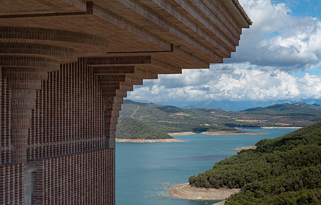 Exterior view of Torreciudad Sanctuary's brick architecture with arches, set against the scenic backdrop of the El Grado reservoir in Spain.