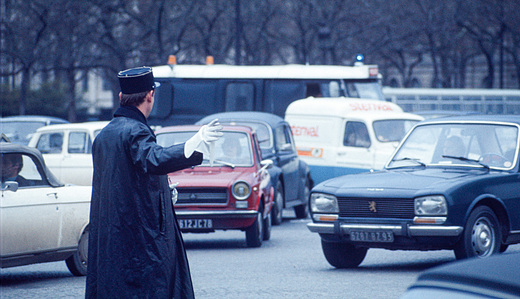 A police officer directs heavy traffic in the centre of Paris, maintaining order amidst the bustling city streets.