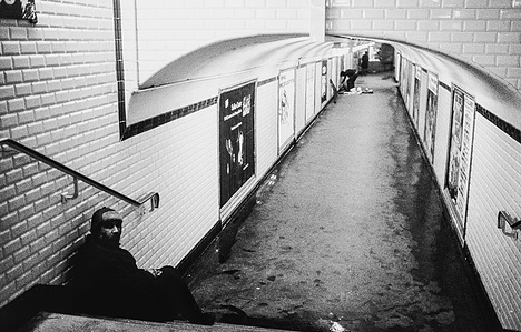 A lone homeless man sitting on the stairs leading to an almost empty platform in the Paris metro lost in thought.
