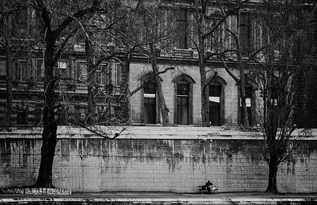 Man sitting alone on a bench by the Seine in Paris, reading a newspaper.