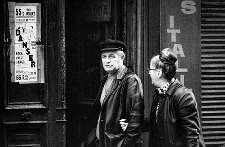 The older couple is walking. The man in a skipper&amp;#x27;s cap glares suspiciously at the photographer while the woman walks beside him, unaware.