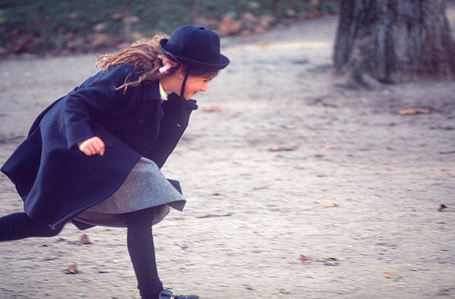 A young girl in a school uniform running and playing in a park in the heart of Paris, full of energy and joy.