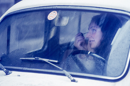 A young woman touches her eyebrows in the rearview mirror before leaving the car.