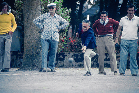 A group of men is playing pétanque in a park in Paris. They are focused on their game in a relaxed atmosphere.