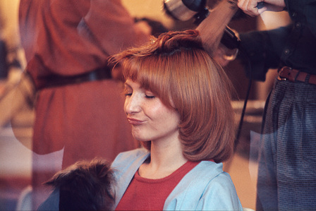A young woman with a small dog on her lap in a Parisian hair salon, having her red hair styled.