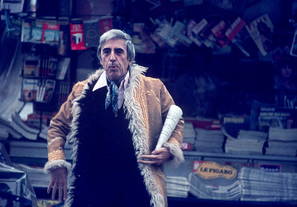 Man in a flamboyant winter coat holding a newspaper purchased from a Parisian kiosk.