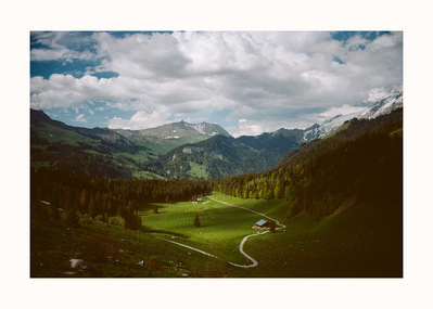 Fine Art print edition of 7 signed & numbered. 50x70 or 30x40 cm on Hahnemühle Bright White paper. Olivier Montay photographer. A grassy valley framed by slopes planted with fir trees, a winding path leads to a chalet. France. Film photography.