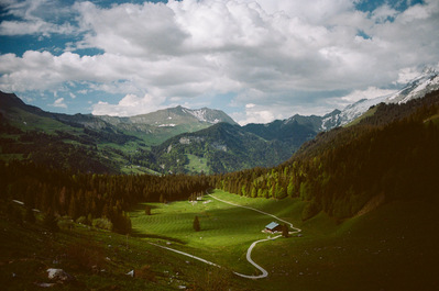 A grassy valley framed by slopes planted with fir trees. At the bottom of the valley, a winding path leads to a chalet. A cloudy sky overlooks the landscape. France, Auvergne-Rhône-Alpes, Haute-Savoie, La Clusaz
Une vallée engazonnée menant à un chalet