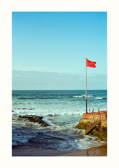 Fine Art print edition of 7 signed & numbered. 50x70 or 30x40 cm on Hahnemühle Bright White paper. Olivier Montay photographer. Moroccan red flag, seafront, waves. Morocco. Film photography