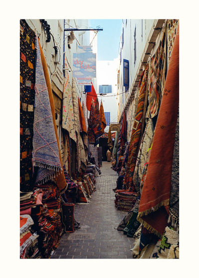 Fine Art print edition of 7 signed & numbered. 50x70 or 30x40 cm on Hahnemühle Bright White paper. Olivier Montay photographer. Cobbled street, lots of colored carpets. Medina. Hoummane Fetouaki St. Morocco. Film photography