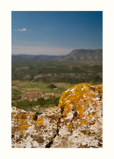 Fine Art print edition of 7 signed & numbered. 50x70 or 30x40 cm on Hahnemühle Bright White paper. Olivier Montay photographer. A stone covered with yellow moss takes up the line of the hilly landscape visible in the background. Occitanie, Tour del far.
