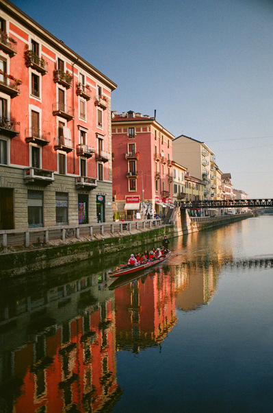 A canal overlooked by pink 4-storey buildings, in the morning light, a thin rowing boat glides on the calm water. Italy, Naviglio Grande di Milano, 2022
Dans le canal bordé d'immeubles roses, un esquif glisse sur l'eau dans la lumière matinale. Milan