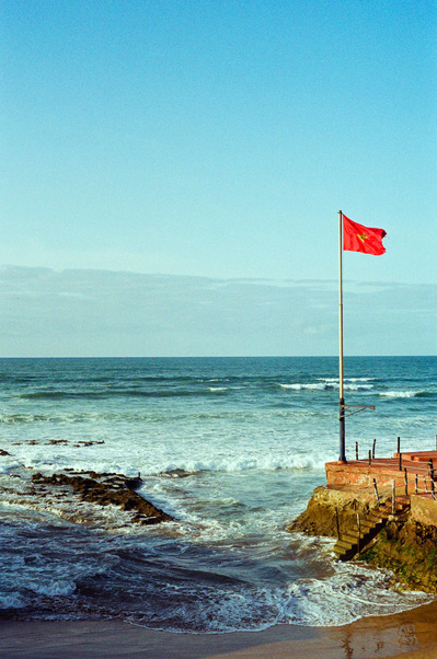 A red Moroccan flag floating in the wind on Casablanca seafront, while waves are crashing on the rocks. Casablanca, Morocco, 2020
Le drapeau marocain flotte au vent sur une plage, tandis que les vagues s'écrasent sur les rochers. Maroc, 29 février 2020