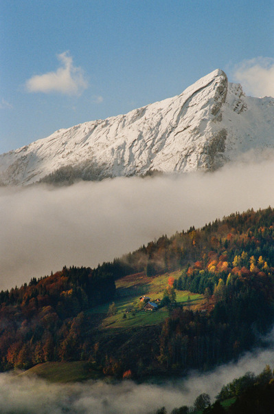 Sunny patches of light on the grassy and coniferous slopes of the mountains, while billows of mist linger in the valleys and a blue sky dominates the snow-capped peaks. France, Auvergne-Rhône-Alpes, Haute-Savoie, Les Clefs, 2021