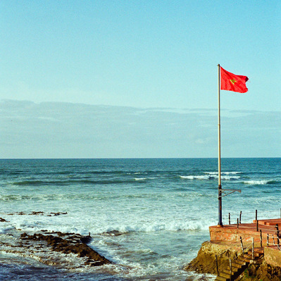 A red Moroccan flag floating in the wind on Casablanca seafront, while waves are crashing on the rocks. Casablanca, Morocco, 2020
Le drapeau marocain flotte au vent sur une plage, tandis que les vagues s'écrasent sur les rochers. Maroc, 29 février 2020