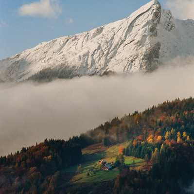 Sunny patches of light on the grassy and coniferous slopes of the mountains, while billows of mist linger in the valleys and a blue sky dominates the snow-capped peaks. France, Auvergne-Rhône-Alpes, Haute-Savoie, Les Clefs, 2021