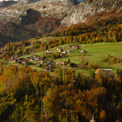 Rocky slopes of Tournette mountain overlook an autumn landscape. Vegetation in brown and orange hues. At the bottom, chalets occupy a clearing of green grass. In the foreground, the concrete church of  Les Clefs. France, Auvergne-Rhône-Alpes, Haute-Savoie