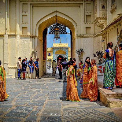 A high quality print available to buy of women dressed in bright orange at the Palace in Udaipur, India filming a Bollywood movie.