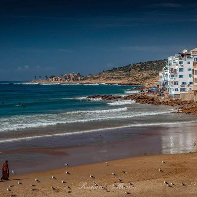 A high quality print available to buy of a man walking a camel along the beach at Taghazout, Morocco.