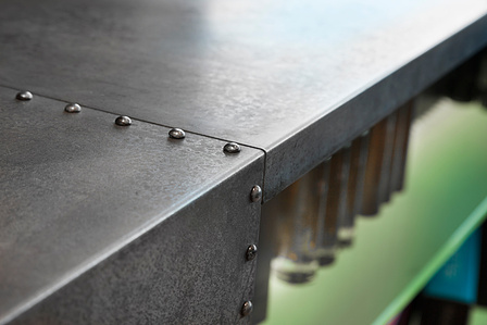 Salon reception desk detail of galvanized sheet metal with steel rivets and back lighted frosted glass shelves