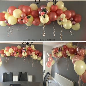 A balloon garland hanging on a wall made with rose gold and ivory balloons.