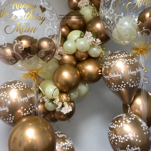 A gold and white balloon garland and two large clear personalised balloons for birthdays. 