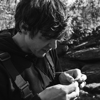 A black and white image of a man attaching a fly to his fishing rod