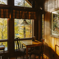 Sunlight streams through large windows, illuminating the interior table of a wooden cabin